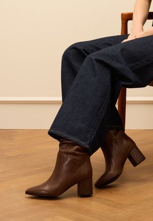 Bruine leren enkellaarsjes met een spitse neus en blokhak, met een slouchy bovenkant en een gladde textuur, gecombineerd met donkere spijkerbroeken.