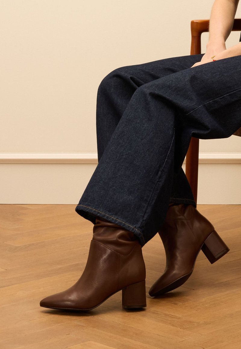 Bottines en cuir marron avec un bout pointu et un talon carré, présentant un dessus flou et une texture lisse, associées à un pantalon en denim noir.