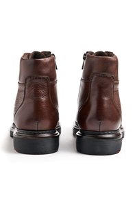 Brown leather ankle boots with a smooth finish, rounded toe, zip closure, and textured rubber sole. Features minimal stitching accents.
