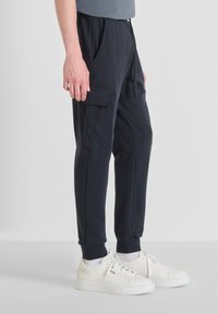 Tamno plave cargo trenirke napravljene od mekog materijala, sa bočnim džepovima, elastičnim pojasom i suženim manžetama, u kombinaciji sa bijelim patikama.