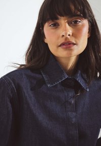 Giacca in denim scuro con colletto, chiusura a bottoni e una sottile texture. Vista ravvicinata che mette in evidenza il ricco colore e i dettagli del tessuto.