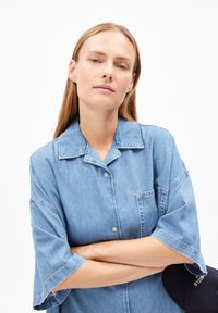 Lichtblauwe denim overhemd met korte mouwen, een kraag en een enkele borstzak. Versleten structuur, knoopsluiting aan de voorkant en losse pasvorm.