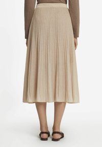 Plissierter Midi-Rock aus hellbeigem Stoff, mit einem taillierten Bund und weicher Textur. Kombinieren Sie ihn mit braunen Sandalen für einen kompletten Look.