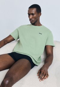 Ανοιχτό πράσινο κοντομάνικο T-shirt με υφή υφάσματος, με μικρό μαύρο λογότυπο "BOSS" στο στήθος. Φορεμένο με μαύρο σορτς.