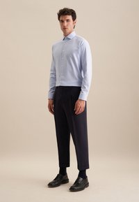 Camicia azzurro chiaro, con bottoni e colletto, abbinata a pantaloni tapered blu scuro e scarpe stringate nere. Tessuto liscio, senza motivi visibili.