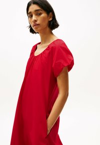 Vestido rojo de corte holgado con mangas cortas abullonadas y escote cuadrado. Hecho de tela ligera con bolsillos laterales. Textura suave.