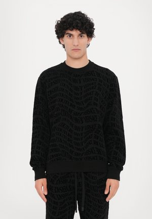 Svart hettegenser med teksturerte, gjentatte logoer. Rund hals, lange ermer og tettsittende mansjetter. Myk stoff, avslappet passform, kombinert med matchende bukser.