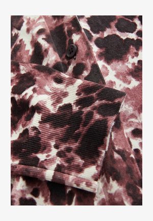 Hladká tkanina tričko v ružovej, krémovej a čiernej leopardiej potlači; má detail čierneho gombíka na prednej strane a textúrované rukávy.