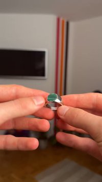 Silberring mit einem rechteckigen grünen Stein auf einer flachen Fassung. Der Ringrand ist glatt mit einer polierten Oberfläche. Hände, die den Ring im Fokus zeigen.