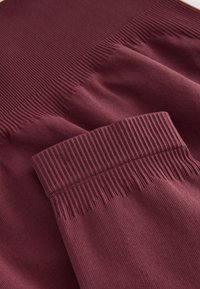 Nærbillede af ribstrikkede vinrøde ærmekanter og taljebånd på et blødt strikplagg, der viser tekstur og sømdetaljer.