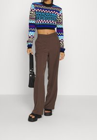 Gehäkelter, verkürzter Pullover mit einem blau, lila und cremefarbenen Schachbrettmuster; braune hochtaillierte weite Hosen; schwarze Plateausandalen.