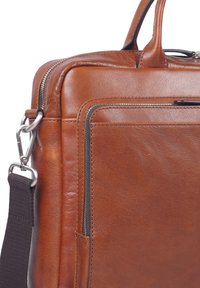 Valigetta in pelle marrone con tasca frontale con zip, zip in metallo, tracolla imbottita e maniglie per il trasporto su sfondo bianco.