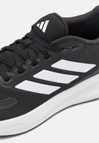 Black athletic shoe made of mesh and synthetic material, featuring white three stripes, a textured design, and "CLOUDfoam" on the sole.