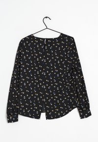 Blusa nera con un motivo floreale in blu, giallo e bianco. Presenta maniche lunghe, un colletto arrotondato e una chiusura con bottoni sul retro.