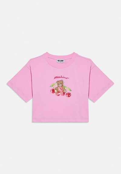 Ροζ κοντομάνικο t-shirt από βαμβάκι, με κεντημένη απεικόνιση αρκούδας που καλύπτει εικονογραφήσεις κερασιών και το κείμενο "Moschino" με καλλιγραφικά γράμματα.