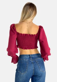 Bordeaux cropped top med puffede ærmer, smocked design bagpå og flæsekanter. Kombineret med medium-høj blå jeans.