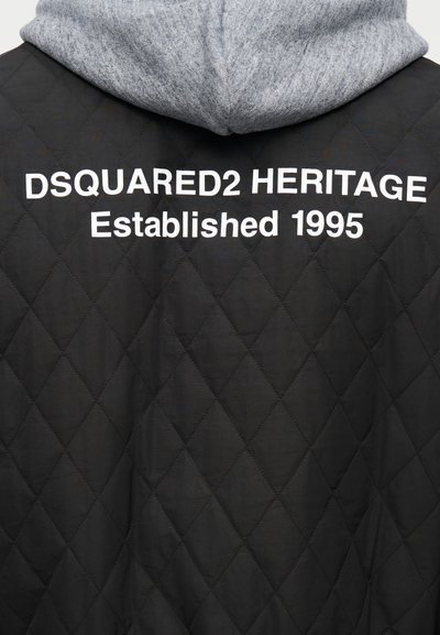 Veste matelassée noire avec capuche grise, portant l'inscription "DSQUARED2 HERITAGE Established 1995" imprimée en blanc dans le dos.