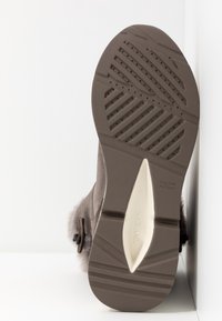 Suola di un boot invernale marrone con marchio GEOX, che mostra i motivi del battistrada, fori di ventilazione e un pulsante laterale su uno sfondo chiaro.