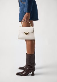 White leather handbag with a structured design, gold hardware, and a top handle, paired with brown leather knee-high boots.