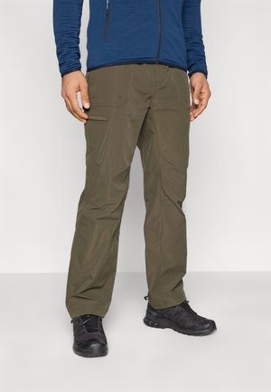 Olivgrüne Cargohosen mit mehreren Taschen, kombiniert mit schwarzen Sportschuhen; dazu ein blaues, langärmliges Oberteil mit Struktur.