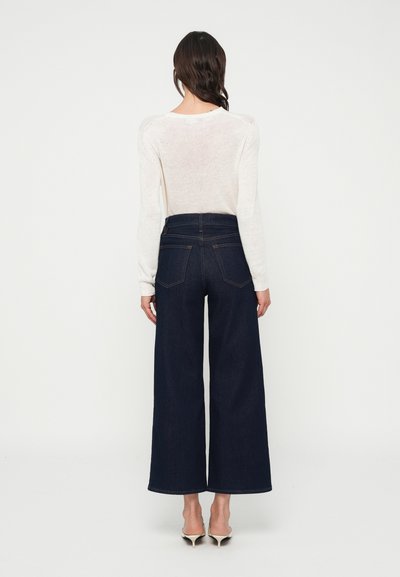 Tumesinised kõrge vöökohaga laia säärega teksapüksid denimist, tagataskudega, kombineeritud heledabeži pikkade varrukatega topsiga.