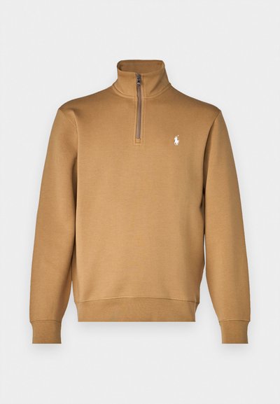 Beige zip-neck sweatshirt, gjord av mjukt tyg, med långa ärmar och en liten vit logotyp på vänstra bröstet. Slät yta.