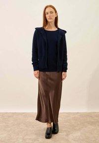 Laivastonsininen vetskarihousupaita, pitkä ruskea satiinihame ja mustat platform-kengät. Sileät pinnat, sovitettu muotoilu ja kerroksellinen tyyli.