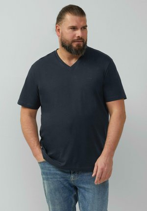 Granatowa koszulka V-neck wykonana z miękkiej bawełny. Krótkie rękawy, luźny krój. Noszona z jasnoniebieskimi dżinsami. Dyskretne logo marki na klatce piersiowej.