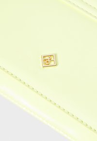 Geantă din piele lăcuită galbenă cu un logo pătrat auriu ce prezintă litere împletite, accentuată cu o cusătură subtilă pe margini.