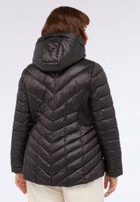 Giacca a vento nera con cappuccio, caratterizzata da un design a chevron e lati testurizzati a pannelli. Materiale liscio e lucido con cuciture trapuntate.