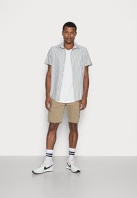 Kurzärmliges Hemd mit vertikalen grauen und weißen Streifen, kombiniert mit beigen Cargo-Shorts und weißen Sportschuhen mit schwarzen Akzenten.