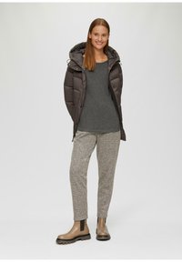 Gevoerde bruine jas met capuchon, grijze langwerpige top, lichtgrijze broek met een patroon en bruine enkellaarzen met elastische zijpanelen.