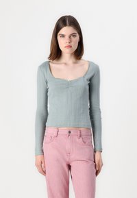 Pitkähihainen, vaaleanvihreä paita, jossa on pyöreä pääntie, ribbikuvio ja keskellä rypytys, yhdistettynä vaaleanpunaisiin ja valkoisiin raidallisiin housuihin.