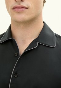 Camicia nera con colletto a punta, piping grigio a contrasto e due bottoni, realizzata in tessuto liscio, che mostra un design pulito e moderno.