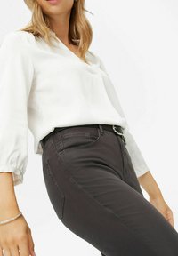 Schwarze Jeans mit schmaler Passform, klassischem fünf Taschen Design, leichtem Stretch und Reißverschluss, kombiniert mit einer lockeren weißen Bluse.