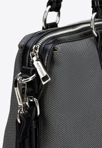 Šedá texturovaná látková kabelka s černými koženými akcenty, stříbrným kováním, dvojitými zipy a přívěskem s logem. Disponuje strukturovaným tvarem.