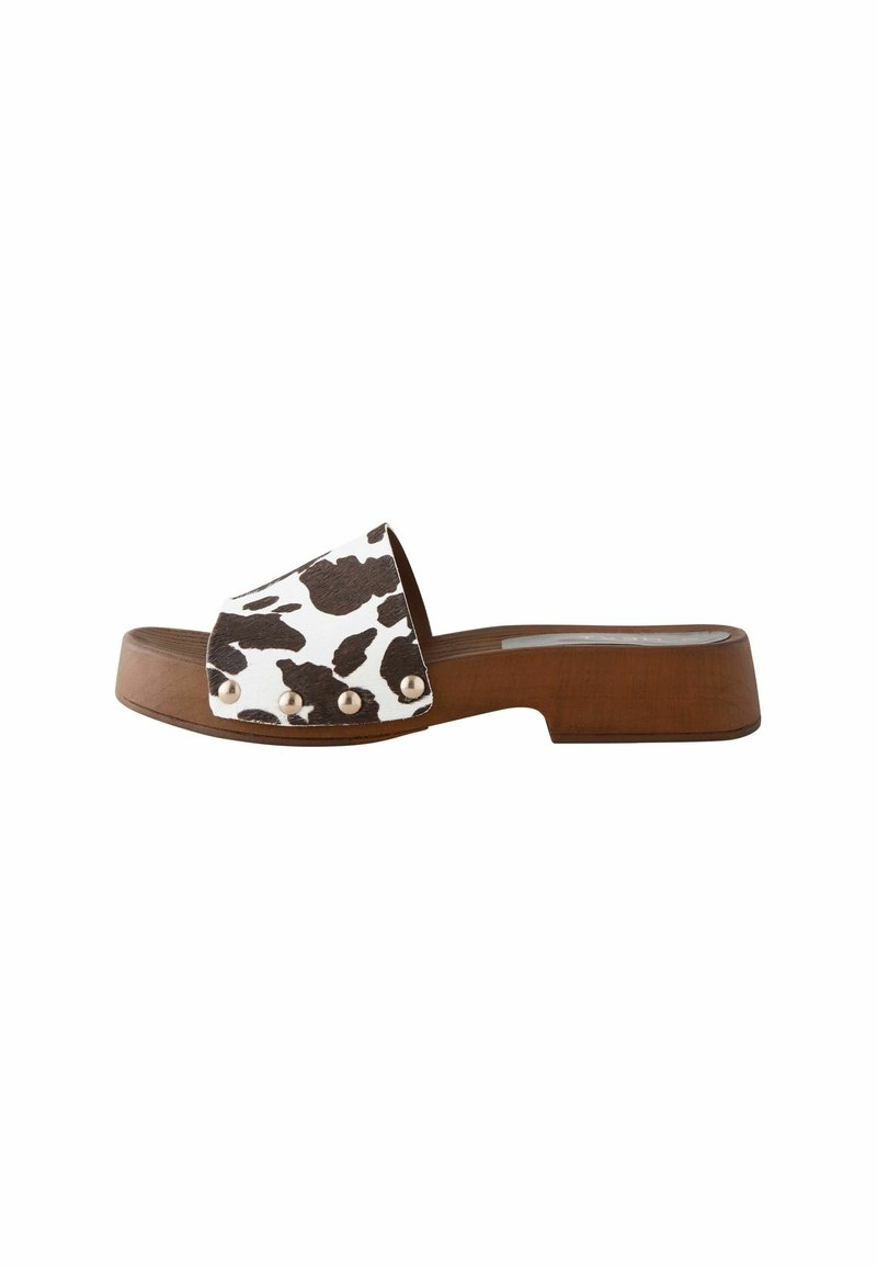 Sandale en bois marron avec une tige imprimée de vache blanche et des clous en métal sur le côté. Semelle plate et design ouvert à l'avant.