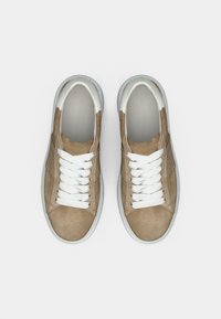 Καφέ σουέτ αθλητικά παπούτσια με υφή και λευκά κορδόνια. Στρογγυλερή μύτη, λευκή ελαστική σόλα και λευκές αντίθετες λεπτομέρειες στη φτέρνα.