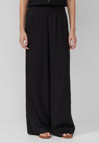 Schwarze, weit geschnittene Hosen mit einer weichen, glatten Textur und einem elastischen Bund, die eine lockere Passform bieten. Keine Taschen oder auffälligen Muster sichtbar.