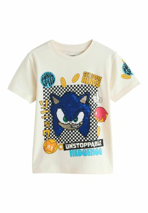 Cremefarbenes T-Shirt mit einer blauen, mit Pailletten bestickten Sonic the Hedgehog Grafik, umgeben von Text und ikonischen Ringen auf einem karierten Hintergrund.