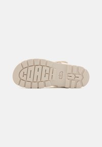 Beige gummisåle med teksturert grep, med hevet "COACH"-logo og tydelig mønster for bedre grep og holdbarhet.