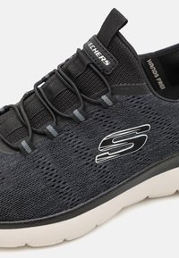 Black athletic shoe with a breathable mesh upper, elastic laces, and a white sole, featuring a side logo and textured accents.