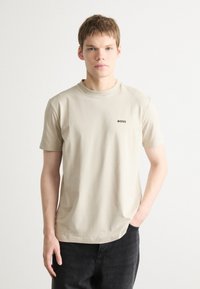 Beige bomulds t-shirt med korte ærmer og rund hals, med et lille sort "BOSS" logo på venstre bryst. Bæret med mørke jeans.