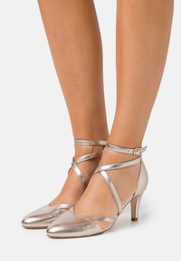 Metalické stříbrné podpatky se špičatou špičkou, páskovým zdobením přes nohu a kotník a úzkým jehlovým podpatkem. Hladká textura.