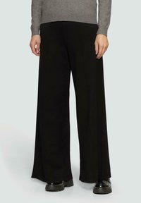 Zwarte wijde broek gemaakt van een zachte stof, met naaddetails en een hoge taille. Gecombineerd met een grijze trui en zwarte plateauschoenen.