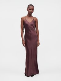 Woman wearing a floor-length sleeveless dark purple satin dress with thin straps, standing against a plain light background.