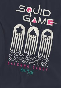 Dark fabric featuring bold white text "SQUID GAME" above three vertical candy shapes—star, triangle, umbrella—paired with "DALGONA CANDY" in pink and green.