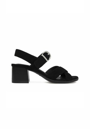 Czarna sandałka na niskim obcasie typu blok z krzyżującymi się przednimi paskami i regulowanym paskiem na kostkę z srebrną klamrą.