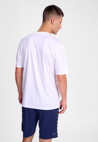 Hvit kortermet treningsskjorte med rund hals, brukt sammen med marineblå shorts med sideakenter. Glatt, lett materiale.