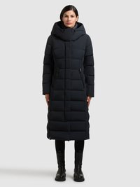 Mörkblå vadderad jacka med huva, som har en lång, rektangulär form, fickor med dragkedja och ett quiltat mönster. Komplett med svarta stövlar.